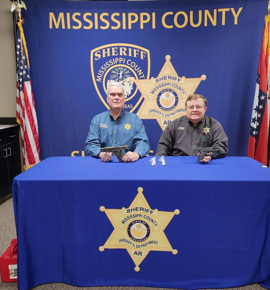 Sheriff Cook posing with Chief Deputy and confiscated drugs and weapons.